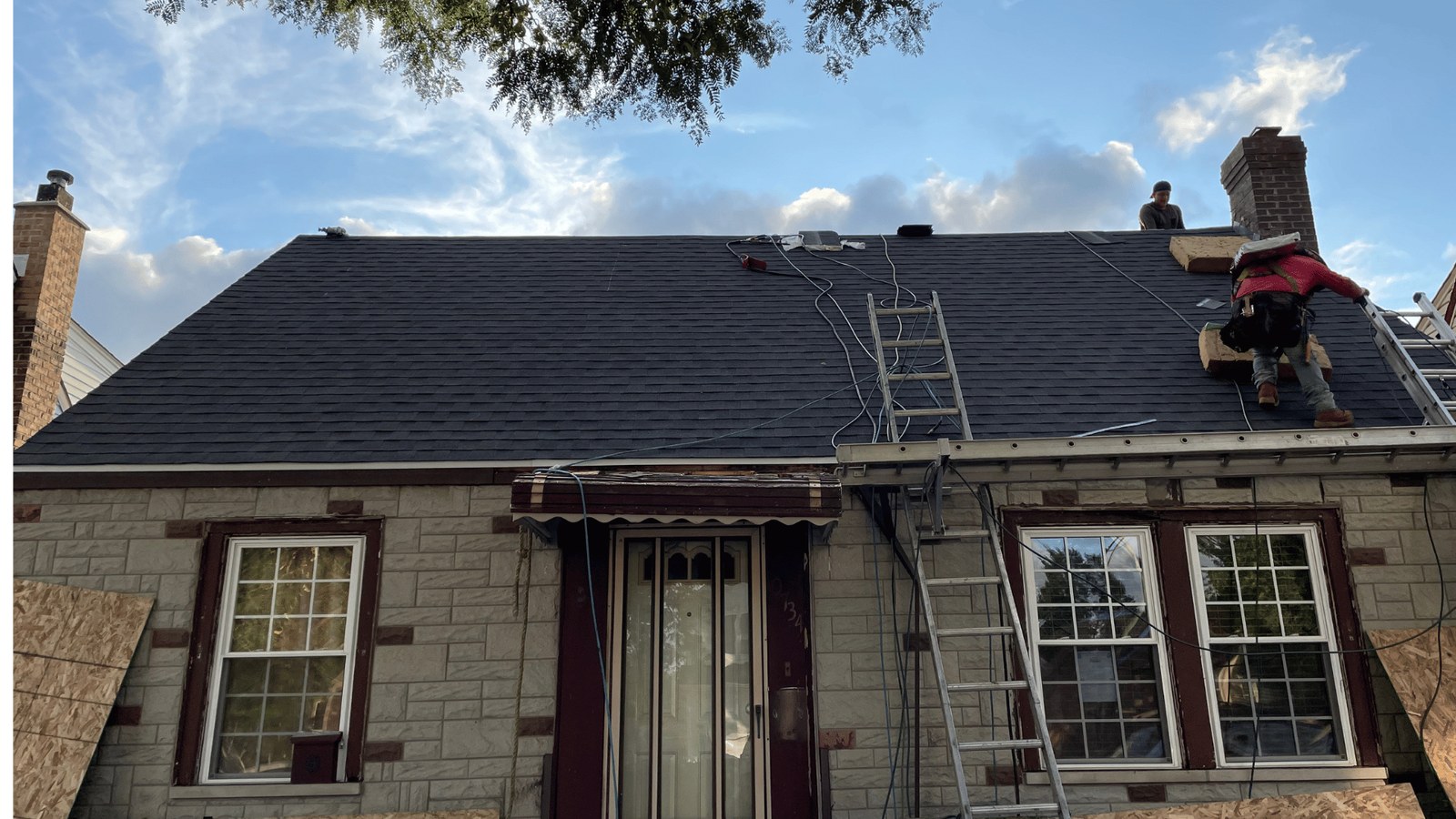 New Origin crew on the roof of a brick Chicago bungalow installing black shingles, ladder at the front