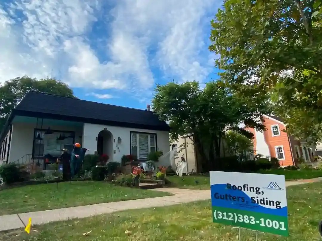 White bungalow with a new black shingle roof and the New Origin yard sign