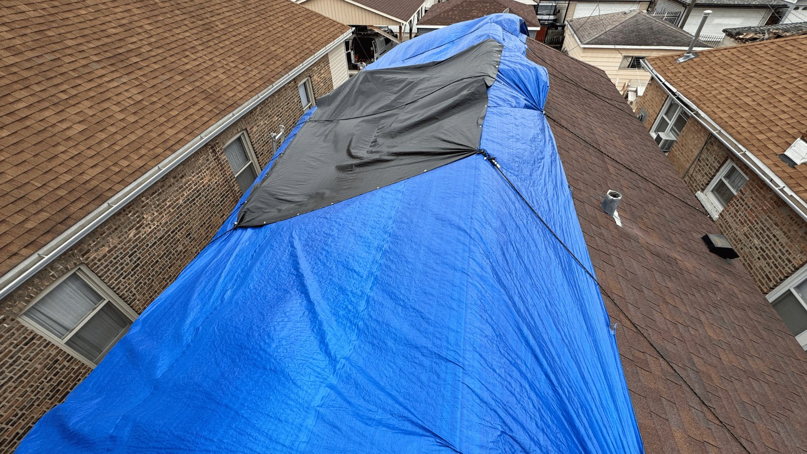 Blue tarp over the roof of a brick Chicago bungalow after storm damage