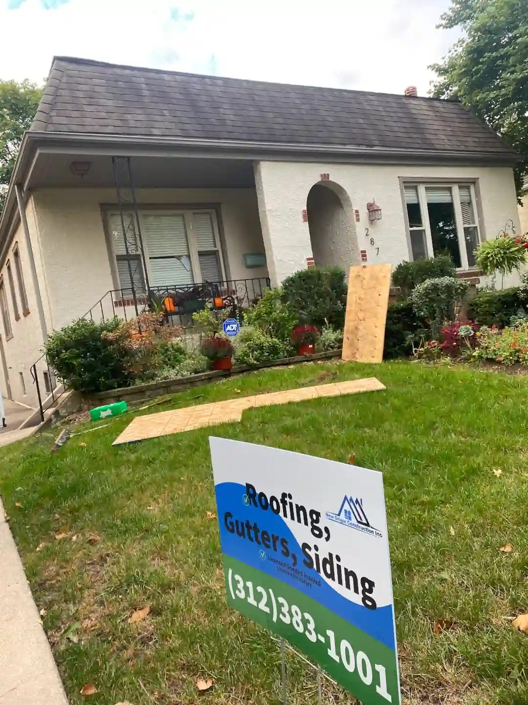 White stucco bungalow with the New Origin yard sign and roofing materials staged on the lawn